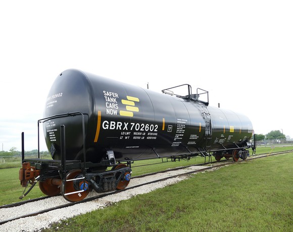 Black tank car on a railroad siding in a green field.