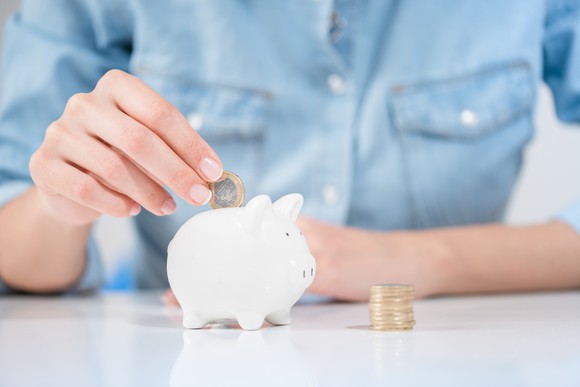 Woman in blue shirt, putting coins in a white piggy-bank.