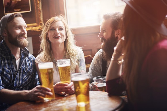 Four young adults talking over beers at a bar.