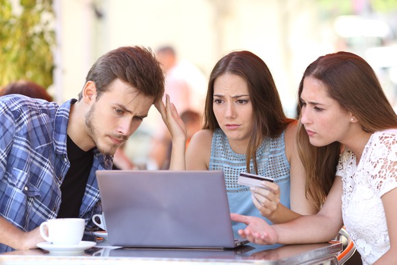 Three friends looking at a computer screen perplexed, as one holds a credit card.