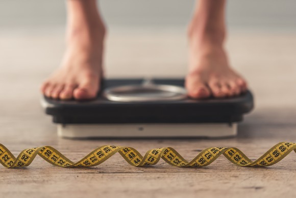 A pair of feet on a scale with a measuring tape in front of it