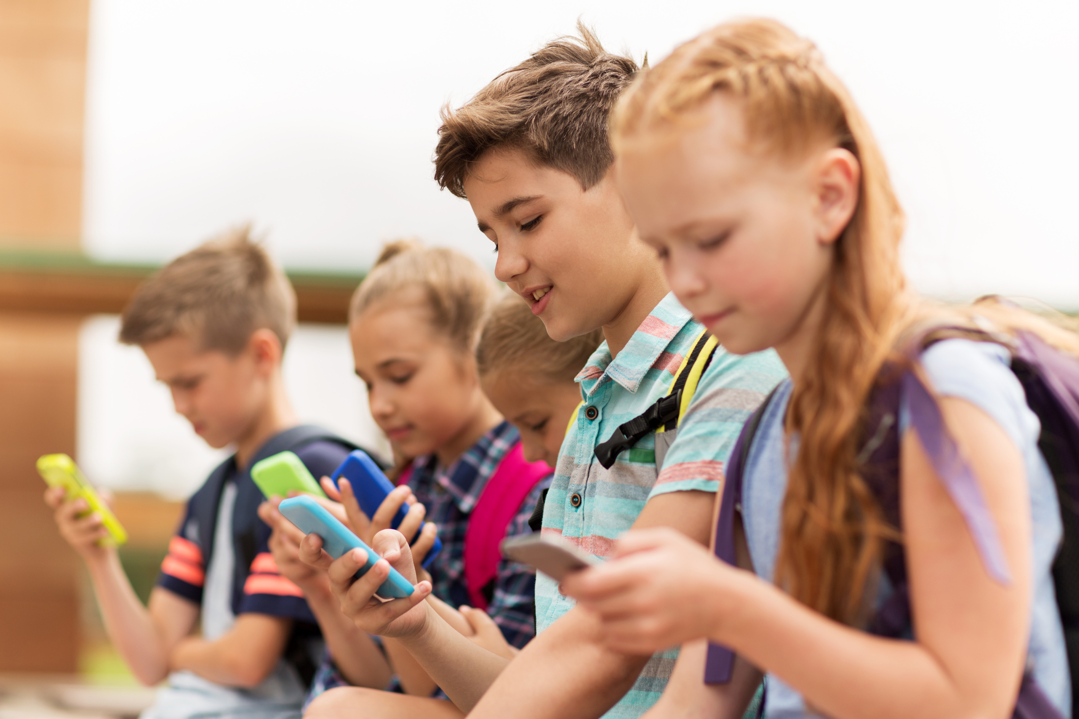 A group of children sitting together, each staring at their own smartphone.