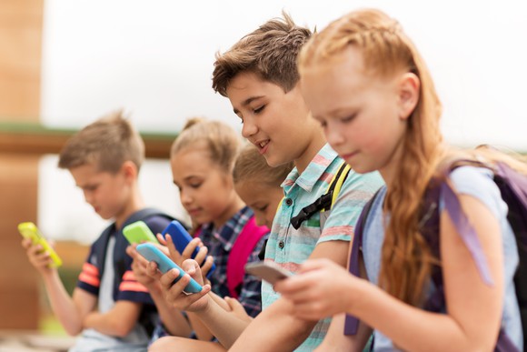 A group of children sitting together, each staring at their own smartphone.