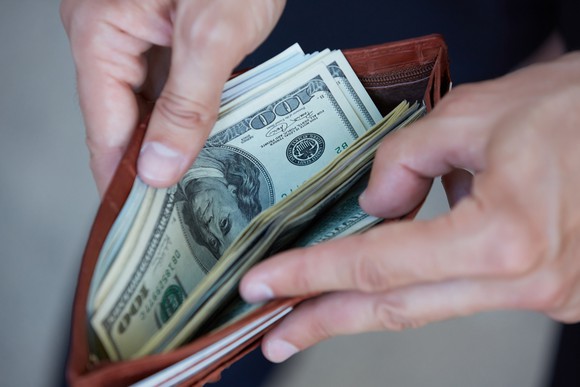 Two hands open a wallet to reveal hundred dollar bills