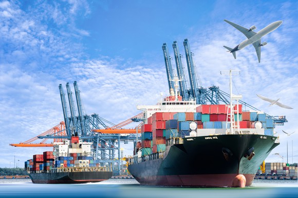 Airplane flying over cargo container ships