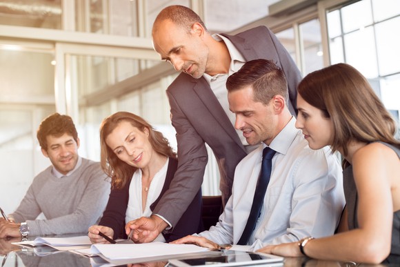 Professional male standing over a group of coworkers, reviewing documents