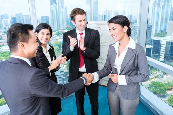 Professional male and woman shaking hands while two other professionals look on and clap