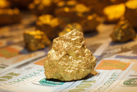 A big gold nugget sitting on $100 bills.