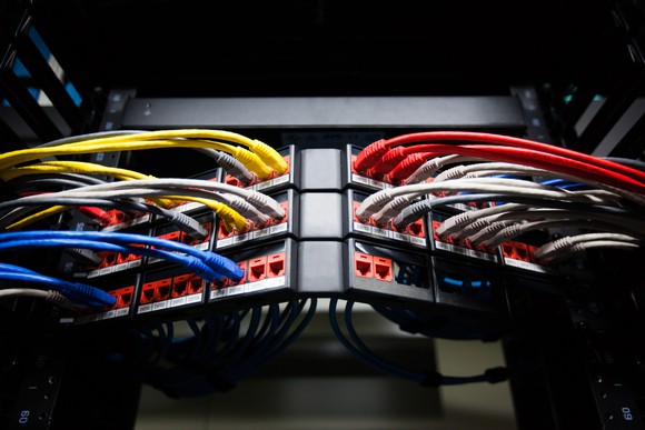 Many brightly colored networking cables, plugged into several switches shown at an angle.