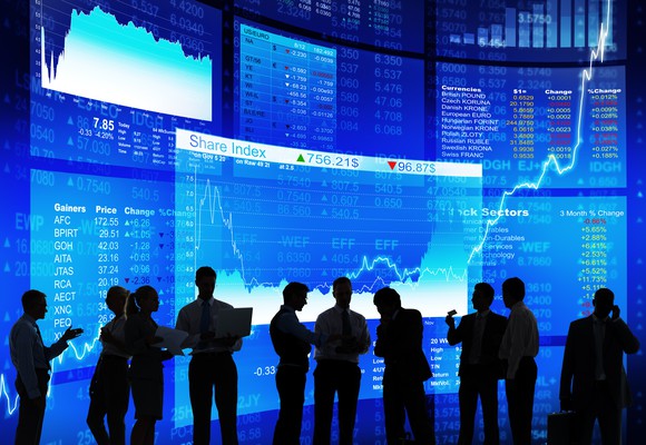 A group of people standing in front of screens displaying stock charts and information.