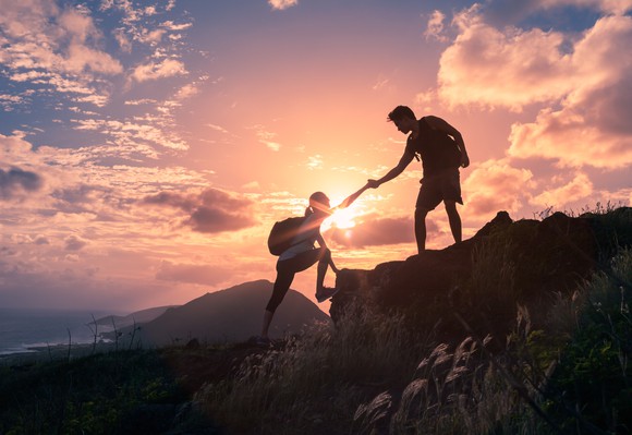 Male and female hikers climbing up a mountain cliff and one of them giving a helping hand