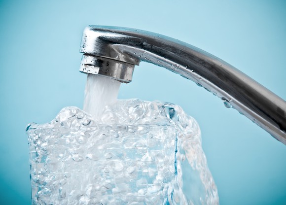 Water from a faucet filling a glass, amidst a light blue background.