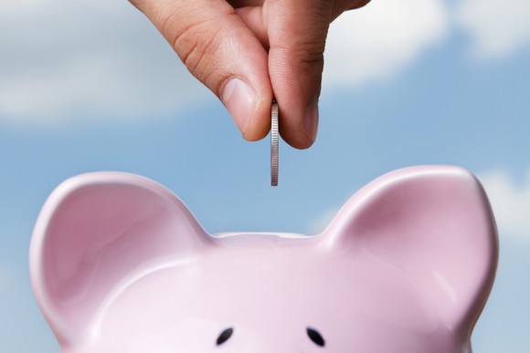 A hand puts a coin into a piggy bank.