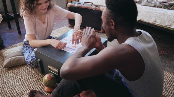 A young couple sitting on the carpet, with a trunk between them, playing a board game.