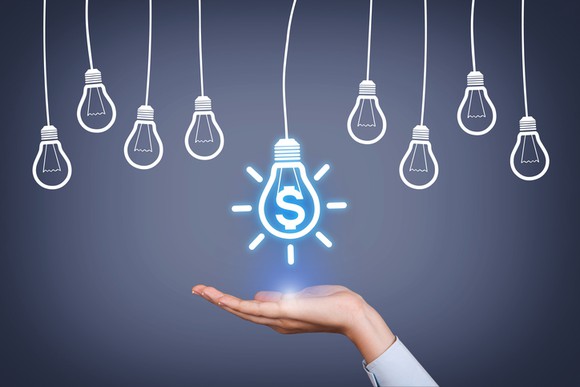 A series of light bulbs drawn on a chalkboard with one in the middle lighting up and someone's hand held flat underneath it.