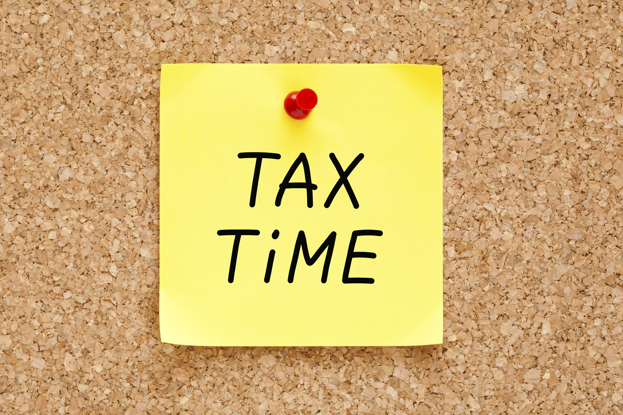 yellow post-it that says tax time, pinned to a bulletin board.
