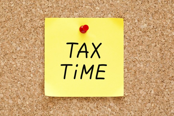 yellow post-it that says tax time, pinned to a bulletin board.