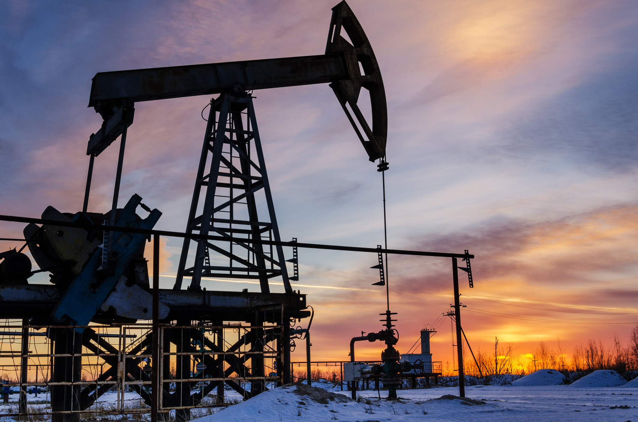 An oil pump with the sun in the background and snow on the ground.