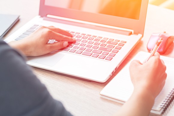 Person typing on a laptop and writing in a notebook
