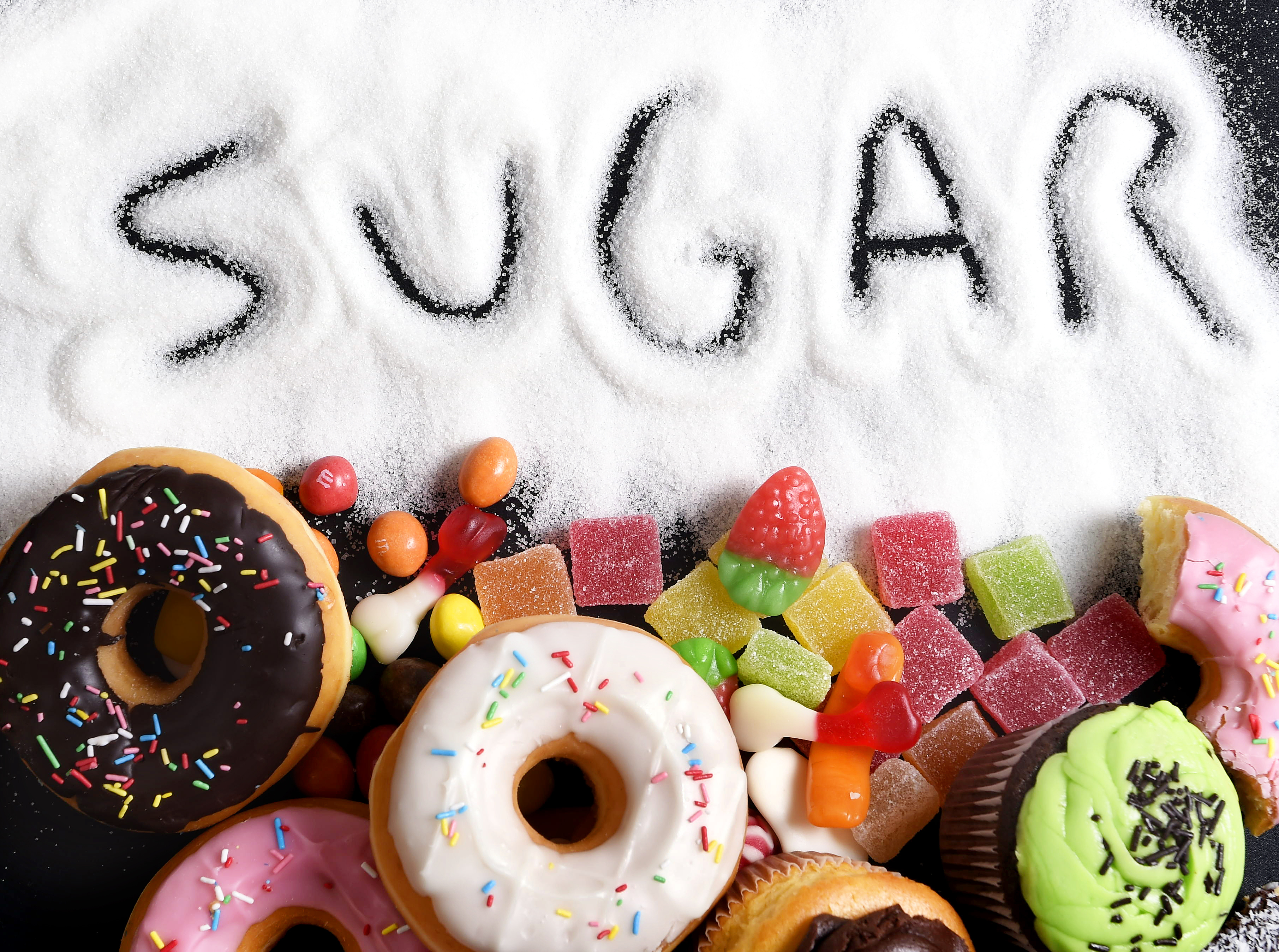 The word sugar drawn out in white sugar, next to donuts and candy.