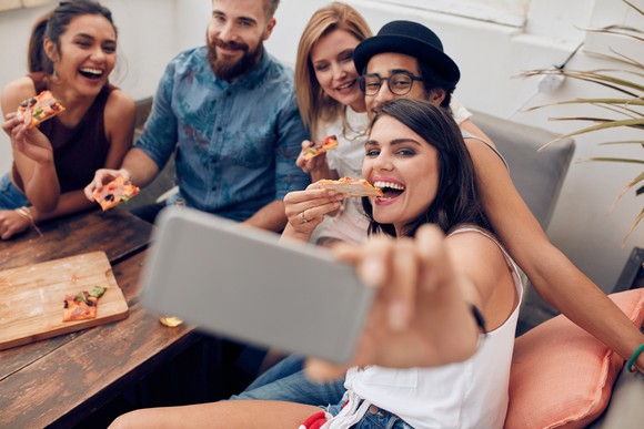 A group of young adults eating pizza and taking a selfie