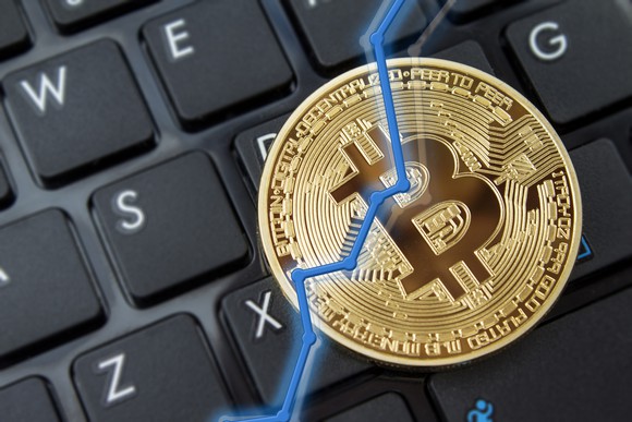 A rising chart overlaid atop a physical gold bitcoin, with a keyboard in the background.