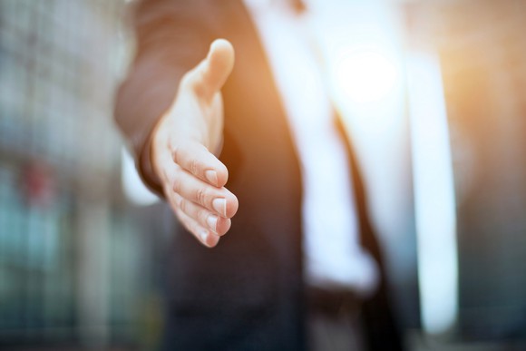 A businessman in a suit stretches his hand out as if to shake someone else's hand.