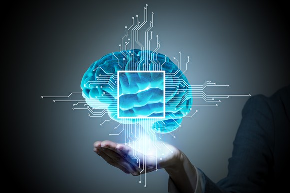 Brain with computer chip on it hovering over a hand.