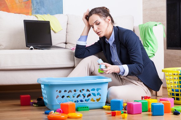 Professionally dressed woman sitting on the floor, cleaning up toys