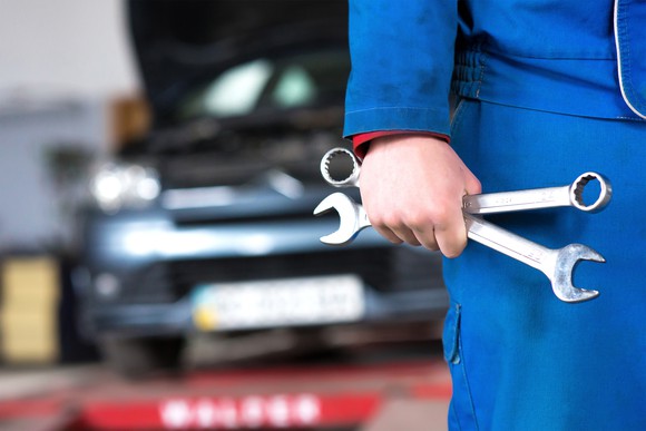 Worker holding two wrenches with a car in the background.