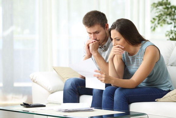 A confused couple going through some papers with a calculator at hand.