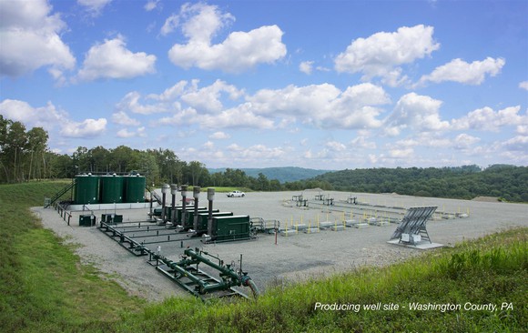 Natural gas well pad in Pennsylvania, including pipe and storage equipment on a gravel square in a grassy field.