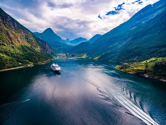 Cruise ship in Norwegian fjord, surrounded by mountains.