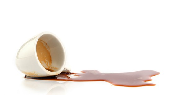 A cup of espresso spilled on a white countertop.