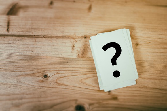 A question mark drawn on a note card that is sitting on a wooden table.