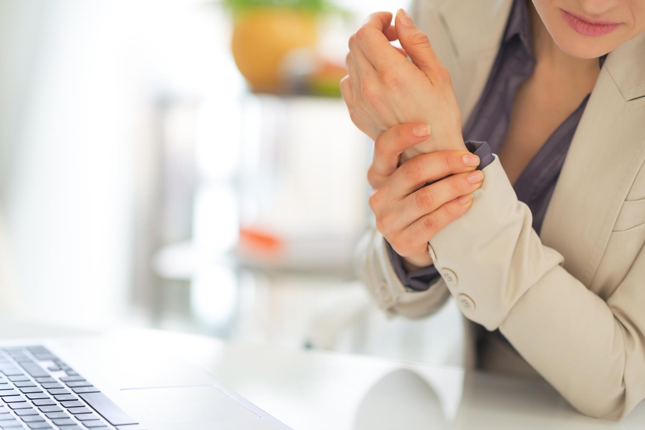 A woman sitting at a desk clutches her wrist.