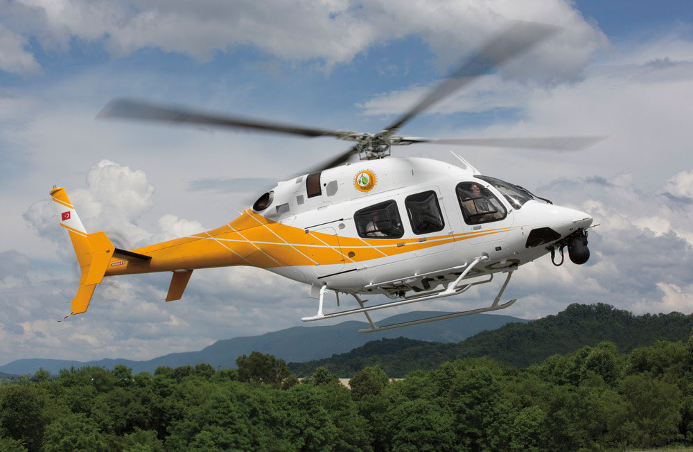 Yellow and white Textron Bell 429 Helicopter flying with mountains in the background
