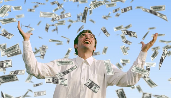 Smiling man with his arms held high as money rains down on him.