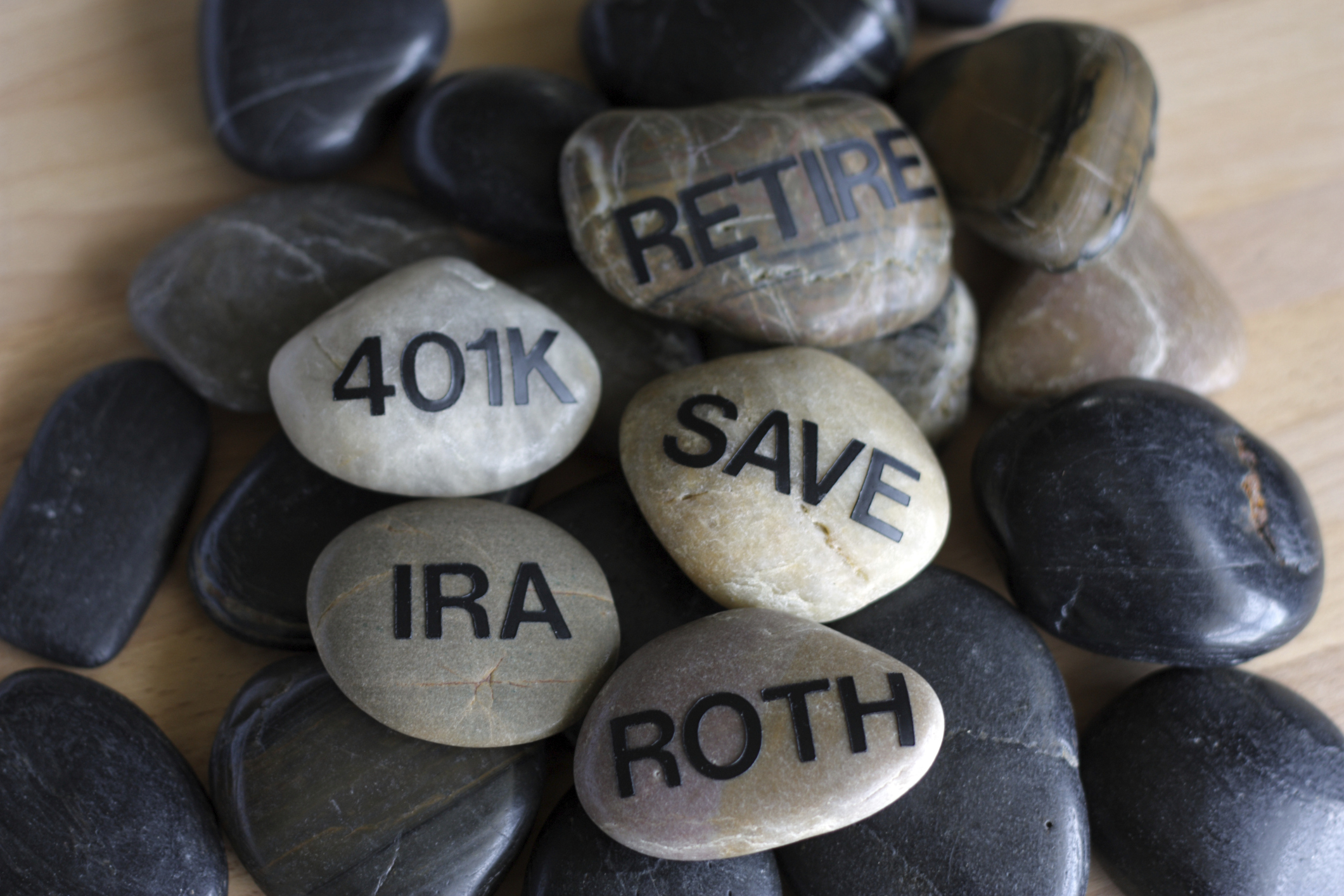 Smooth stones with words written on them such as retire, 401k, IRA, Save, and Roth.