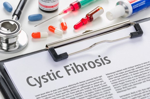 Paper on clipboard with Cystic Fibrosis written on it surrounded by medication and a stethoscope