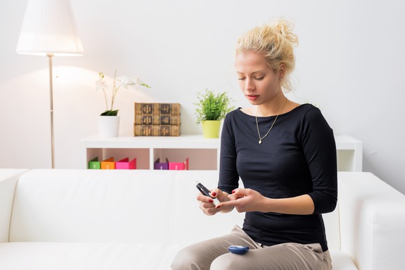 Woman sitting on couch checking her blood sugar levels