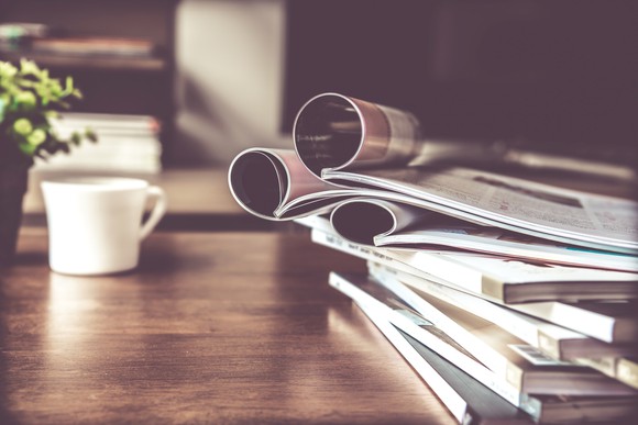 A cup and stack of magazines on a table