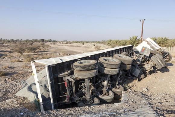 A flipped over semi-truck on the side off the road.