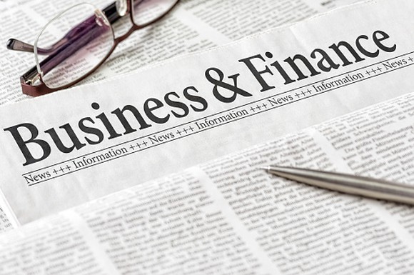Close-up of the business and finance section of a newspaper, with a pen and a pair of glasses.