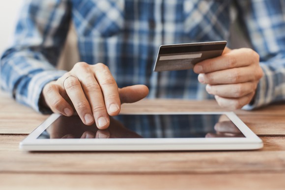 A man holds a credit card as he prepares to make a purchase on a tablet.