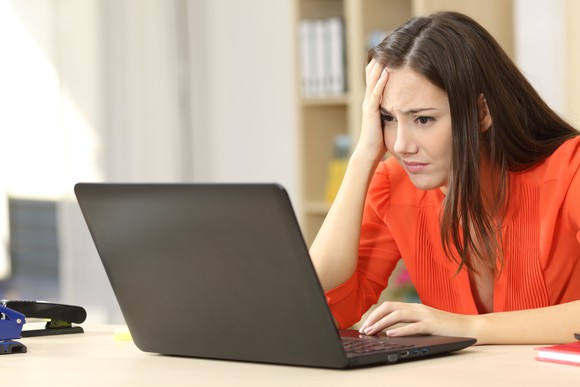 Woman holding her head while looking at a laptop in frustration