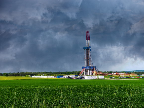 Drilling rig in field with clouds in background.