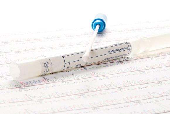 A tube containing a swab for a genetic test, lying atop a graph of test results.
