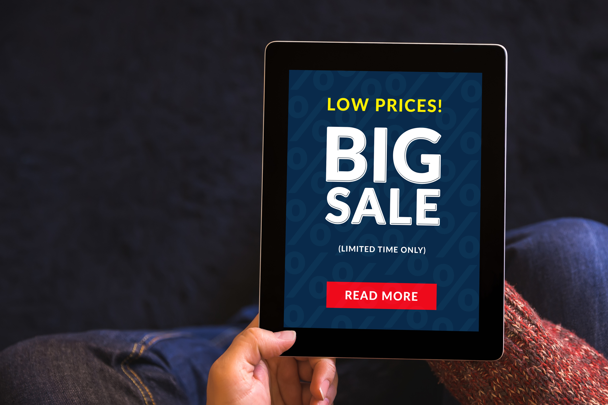 Hands holding a tablet computer with big sale writing on the screen.