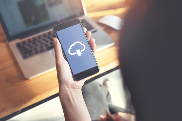 A closeup of a person holding a smartphone with a symbol of a cloud downloading.